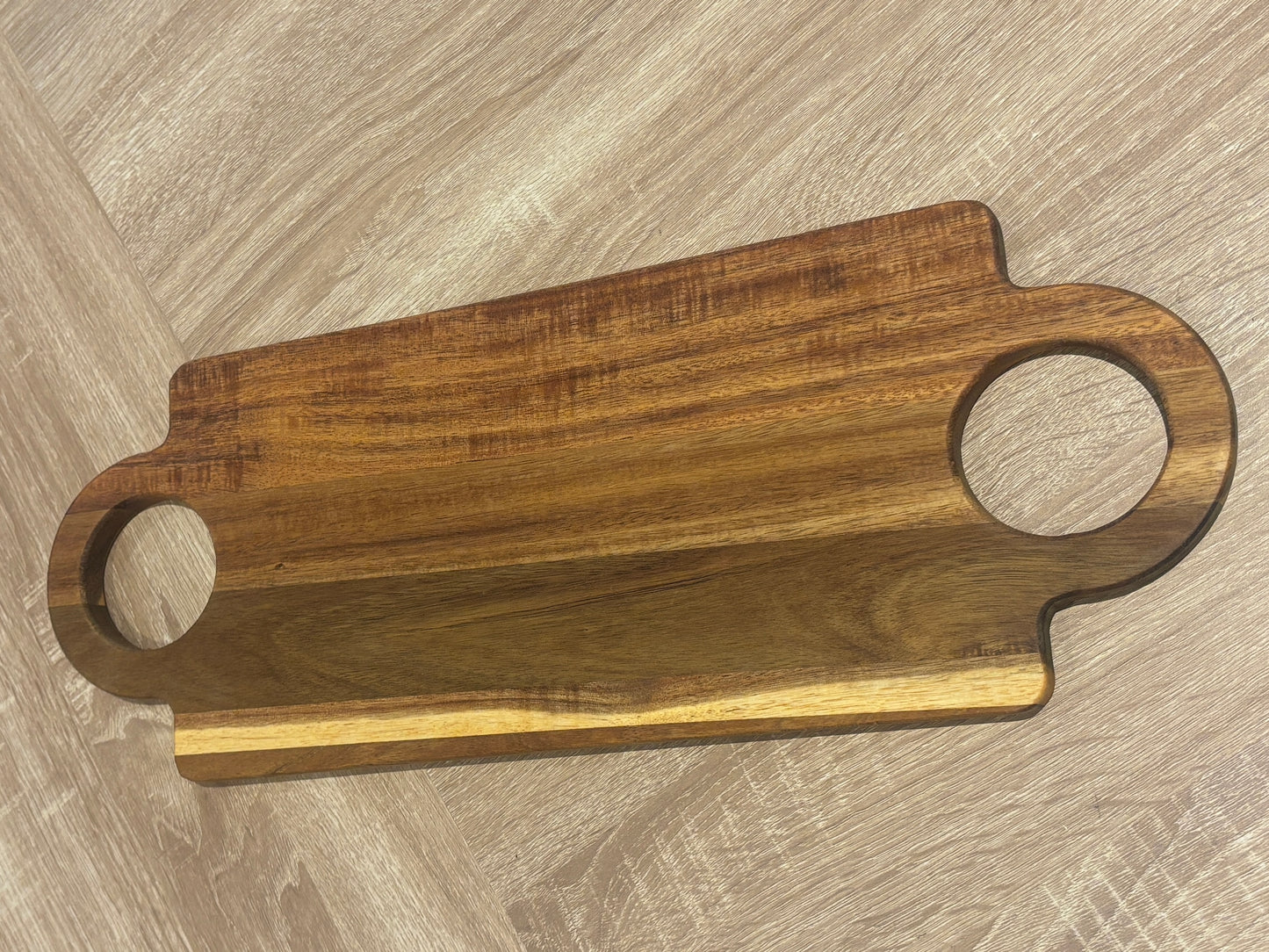 Wooden cutting board with handles on a wooden surface