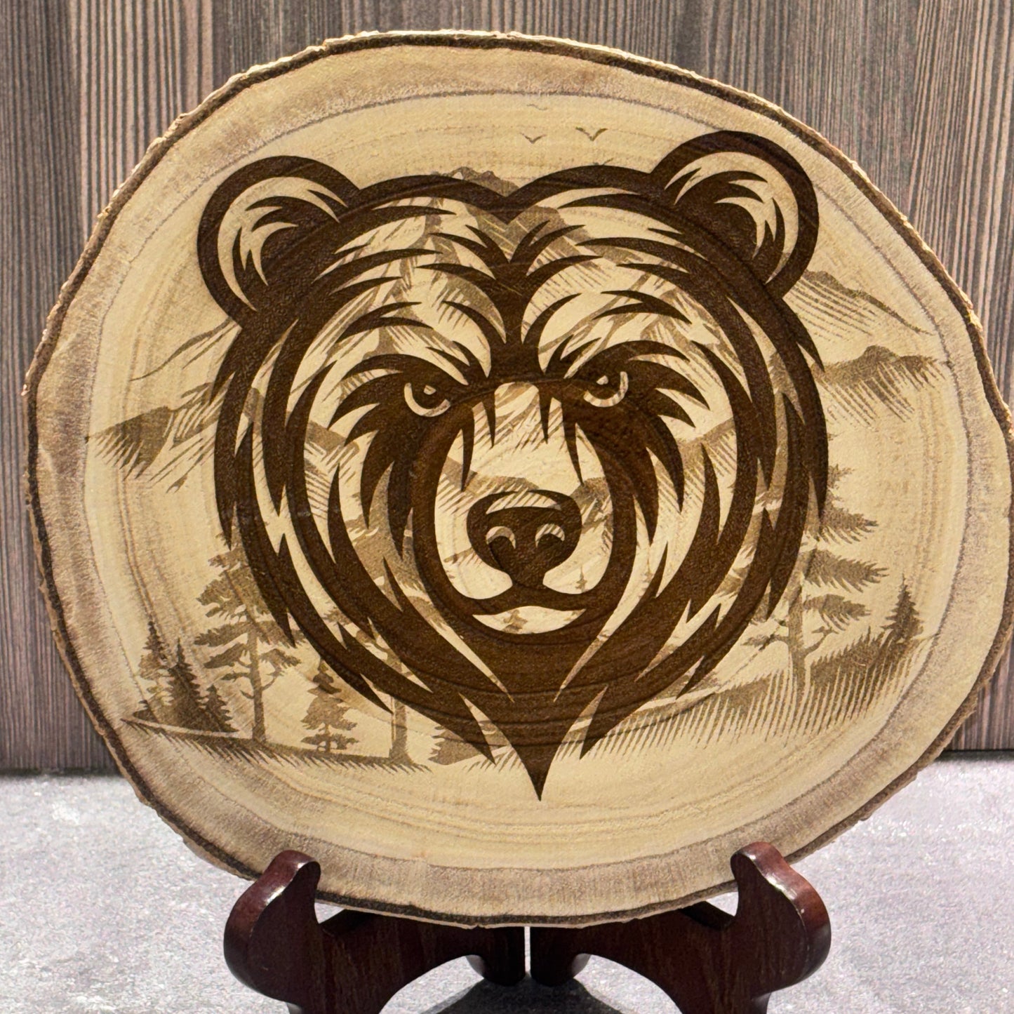 Natural 8 to 9 inch wood slice engraved with a bear portrait over a mountain and forest landscape. Stand not included.