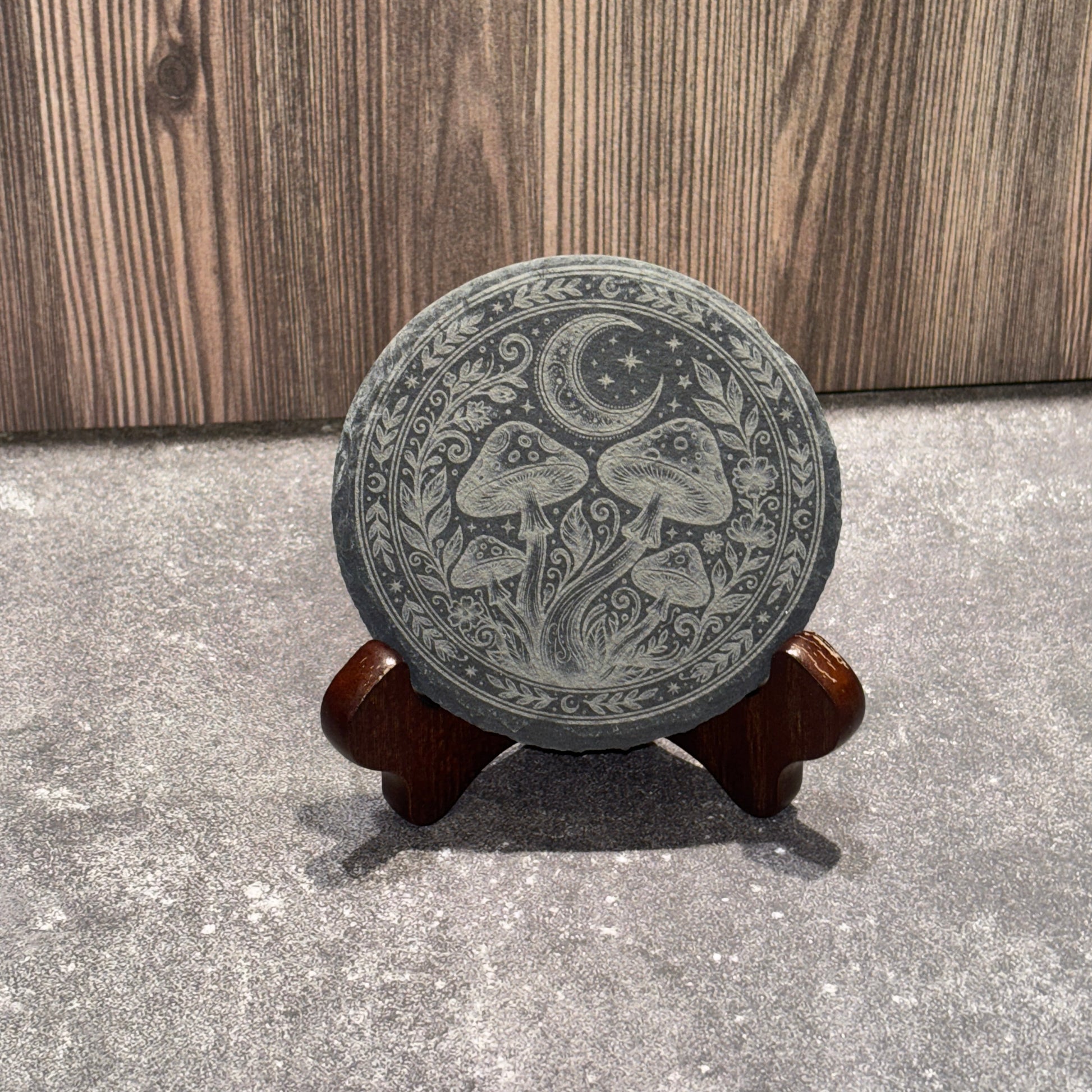 Decorative slate coaster with intricate design on a concrete floor.