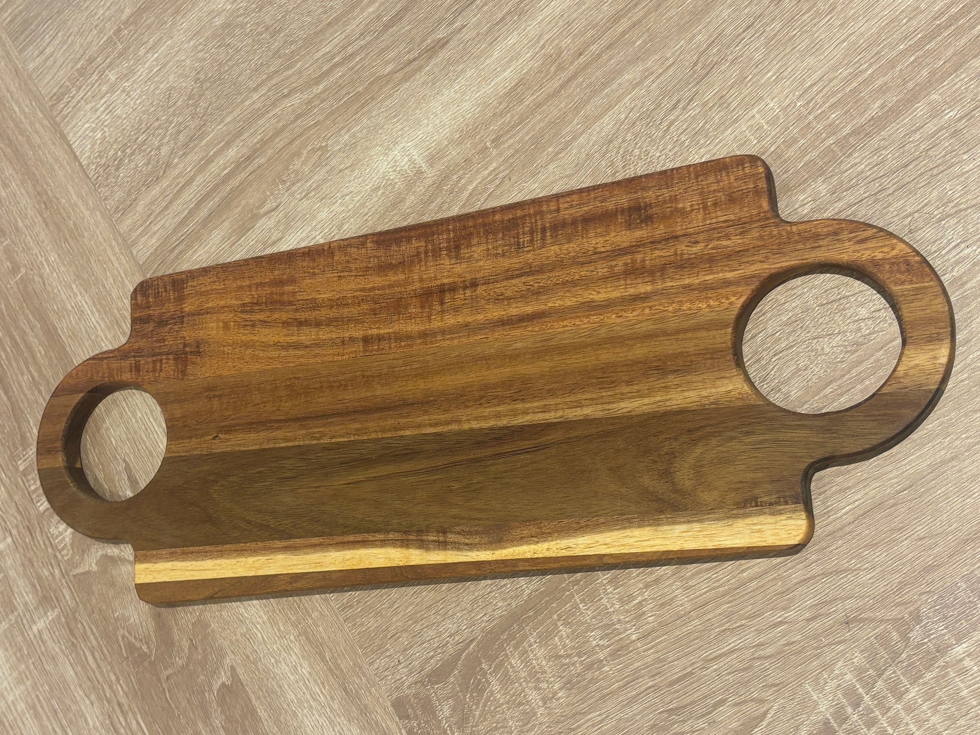 Wooden cutting board with handles on a wooden surface