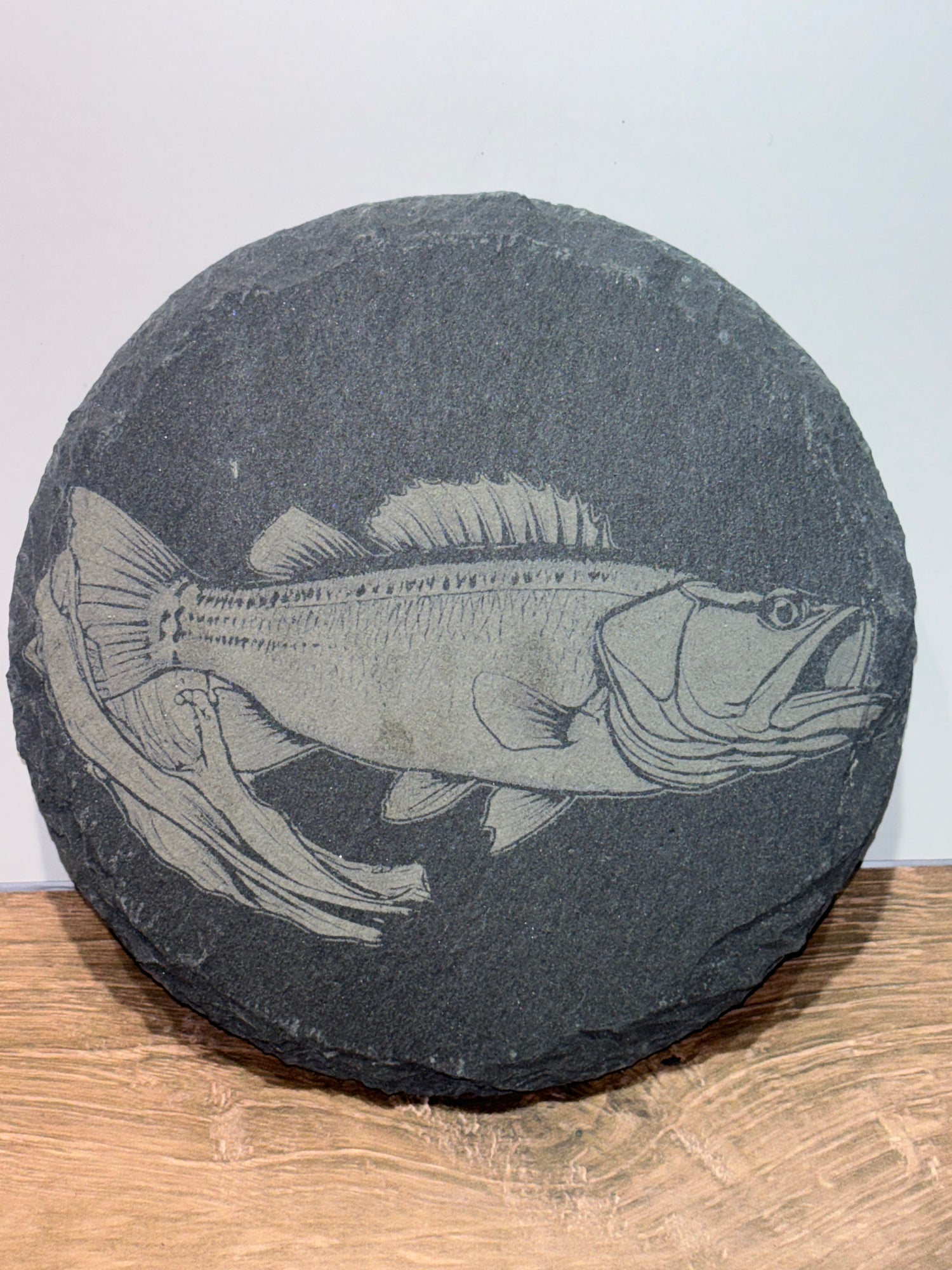 Round 4 inch black slate coaster engraved with a detailed fish swimming near underwater reeds.