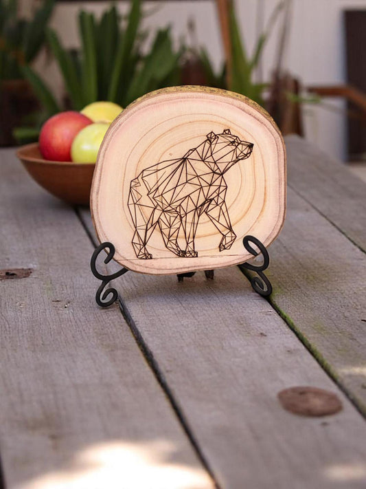 Wooden circular light with geometric bear design on a stand, placed on a wooden surface with apples in the background.