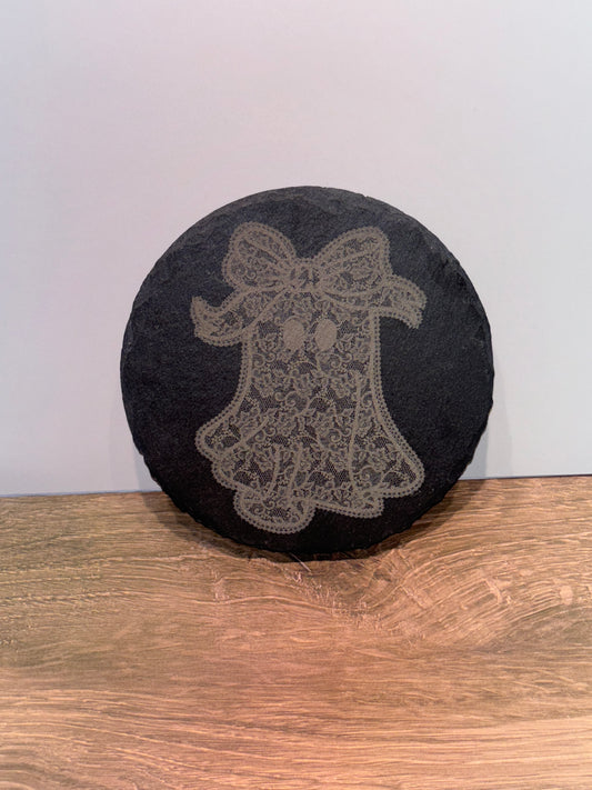 Round natural slate plaque featuring a laser-engraved lace-style ghost with a bow, displayed on a wooden surface.