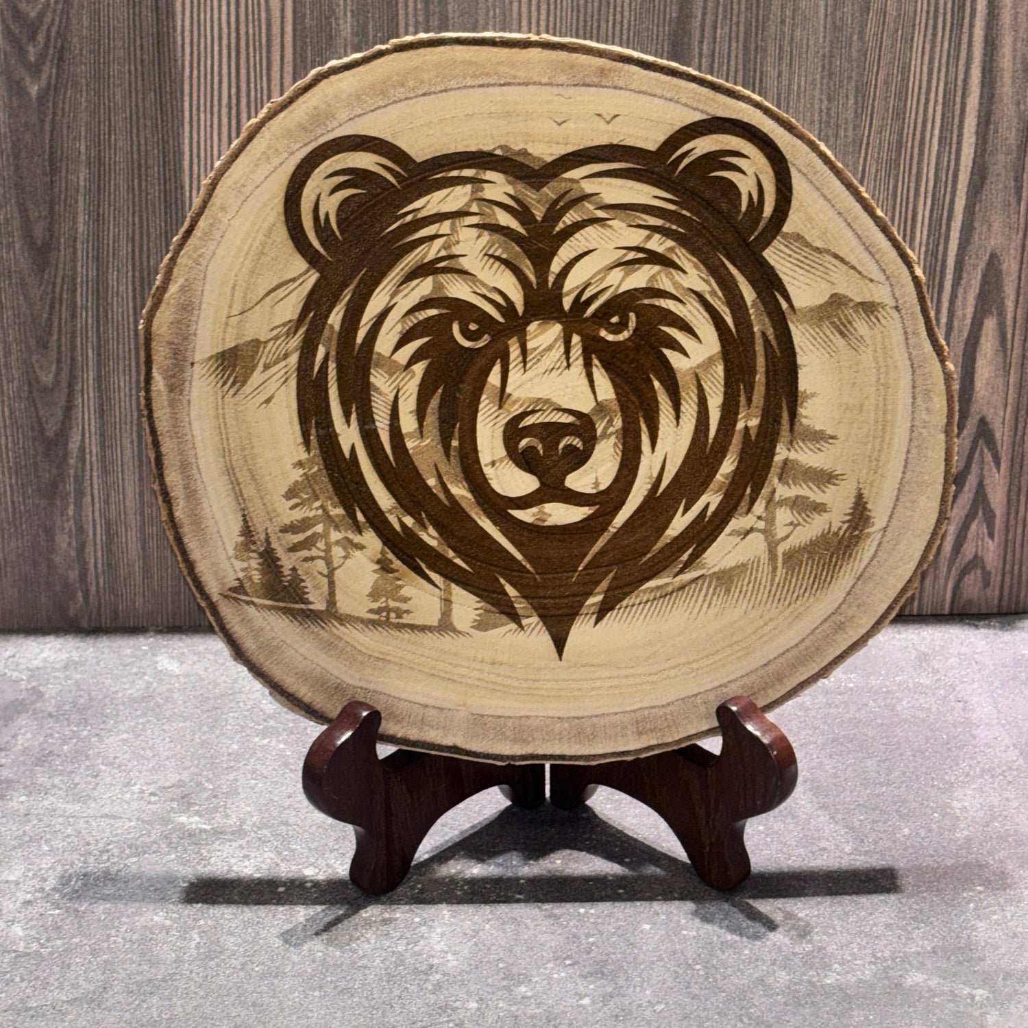 Natural 8 to 9 inch wood slice engraved with a bear portrait over a mountain and forest landscape. Stand not included.