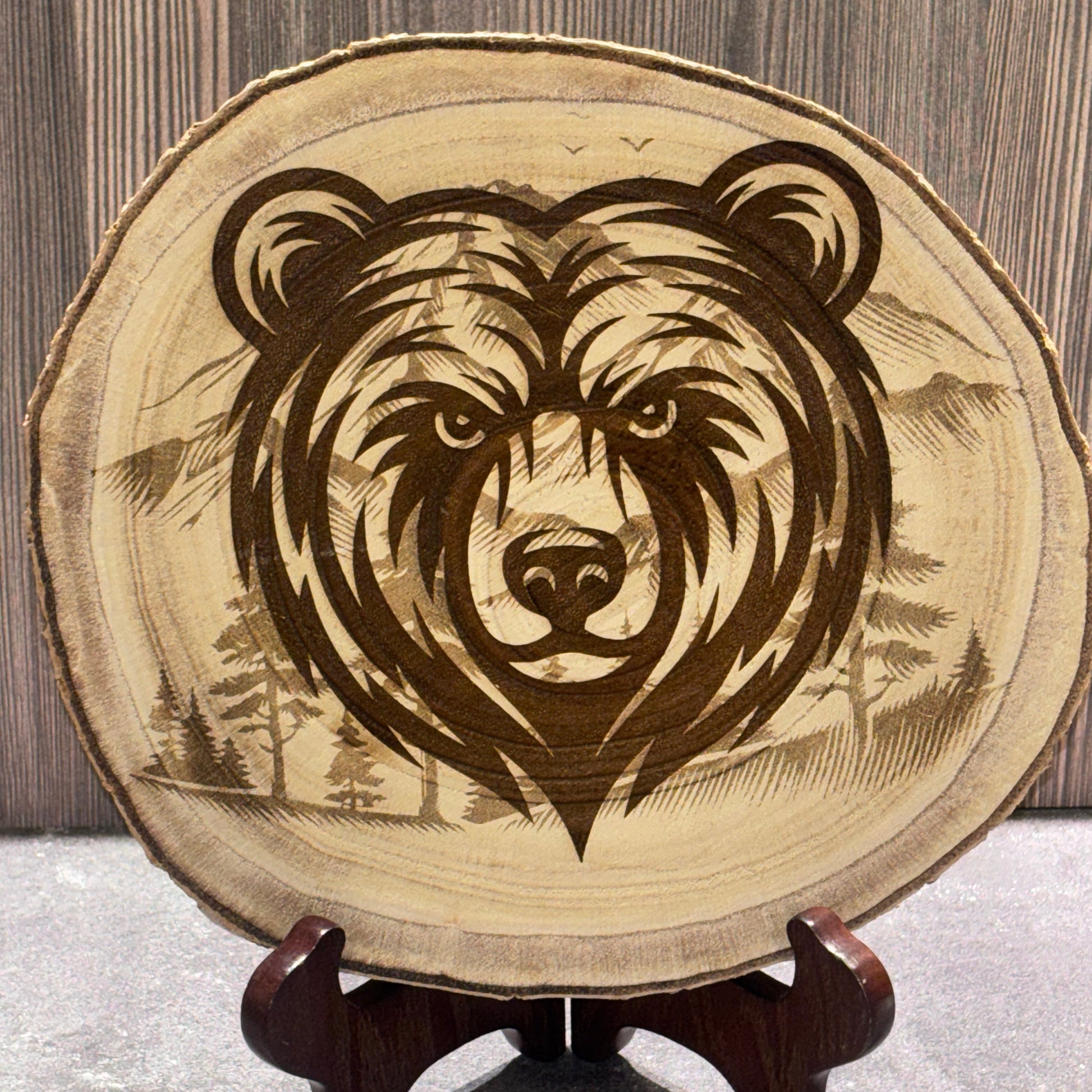 Natural 8 to 9 inch wood slice engraved with a bear portrait over a mountain and forest landscape. Stand not included.