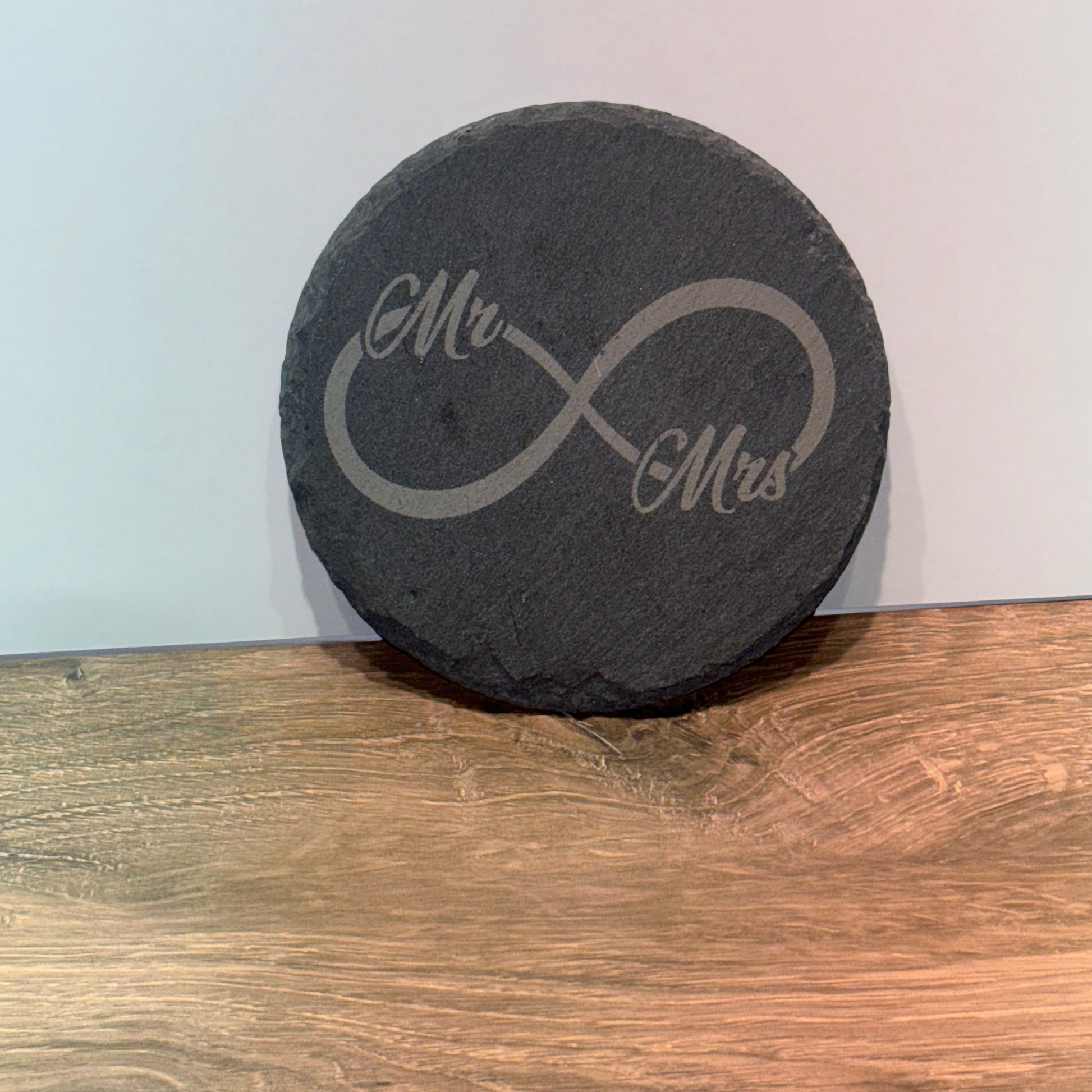 Round black slate coaster engraved with an infinity symbol connecting the words "Mr" and "Mrs."