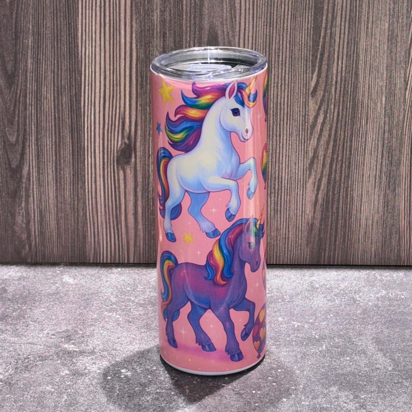 Pink tumbler with unicorn design on a wooden surface