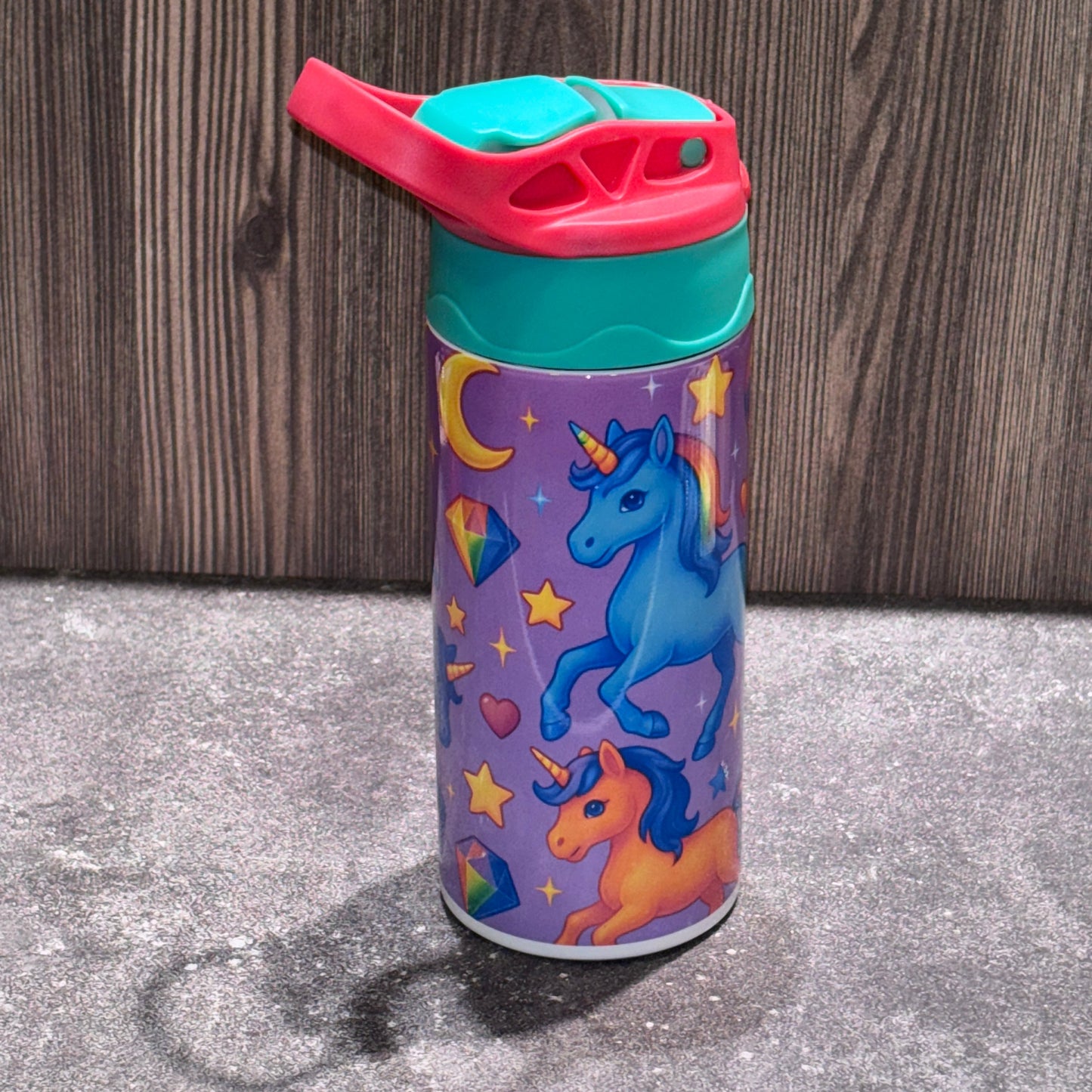 Colorful tumbler with unicorn design on a wooden surface and concrete floor.